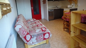 Un espace de vie compact comprenant un coin cuisine, un canapé, une table à manger et une porte rouge.