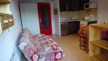 Un espacio habitable compacto con kitchenette, un sofá, una mesa de comedor y una puerta roja.