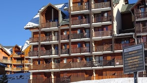 Un immeuble en bois à plusieurs étages, doté de balcons, avec une piste de ski en arrière-plan et un panneau indiquant qu’il est interdit de se garer.