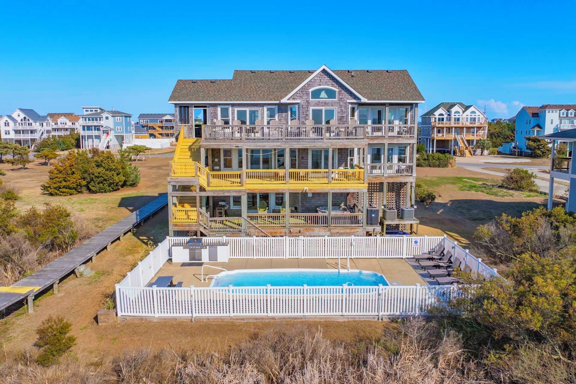 A multi-story beachfront property with a pool, balconies, and a wooden deck.