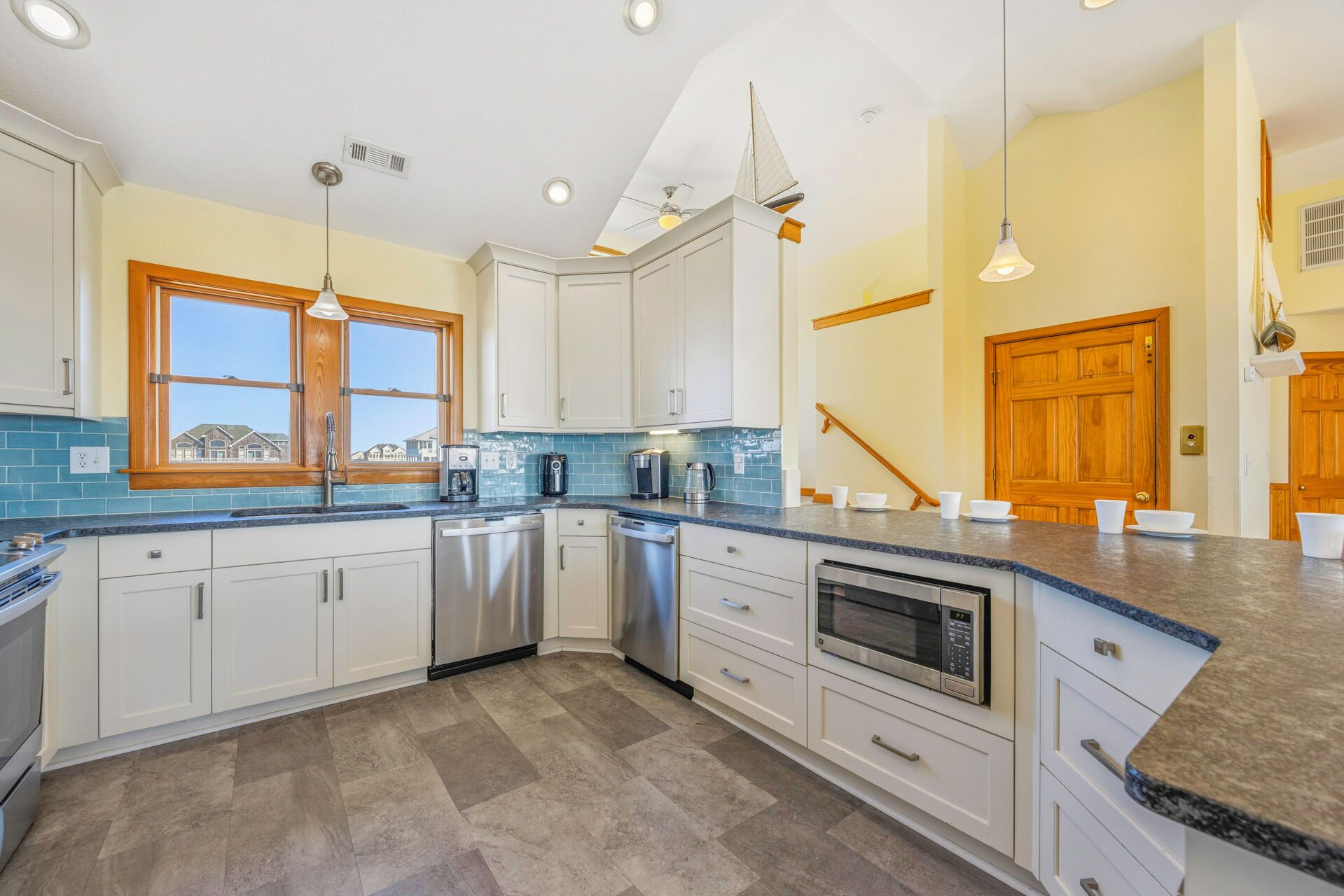 A kitchen with white cabinets, a granite countertop, a dishwasher, a microwave, and a large window.