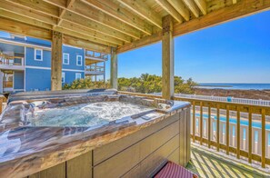 A hot tub on a wooden deck with a view of the ocean and a building in the background.