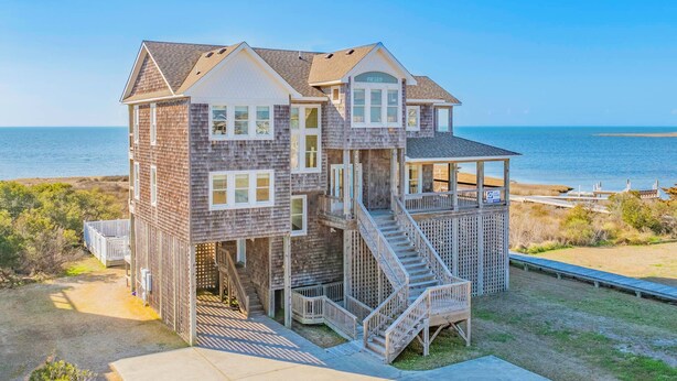 A multi-story wooden house with a balcony, a staircase, and a view of the ocean. - Sweet Tranquility – Soundfront Retreat w/ Pool, Hot Tub, Game Room & Tiki Bar (Salvo)