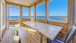 A covered outdoor area with a wooden table and benches, large windows, and a view of the beach and ocean. - Sweet Tranquility – Soundfront Retreat w/ Pool, Hot Tub, Game Room & Tiki Bar (Salvo)