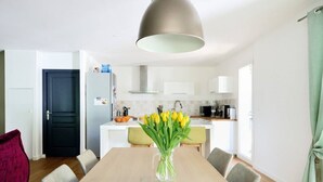A modern kitchen with white cabinets, a black refrigerator, and a dining area with a wooden table and chairs. - PRETTY FAMILY HOUSE IN PROVENCE (Éguilles)