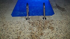 Piscina com um recurso aquático iluminado em azul, cercada por um deck ladrilhado e guarda-corpo de metal.