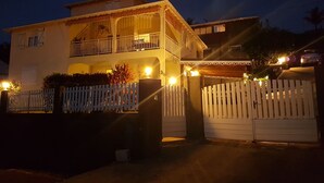 Uma casa de dois andares com varanda, cerca branca de piquete e portão fechado.