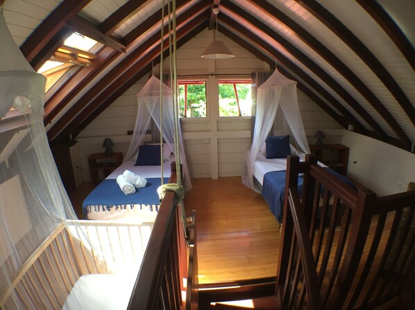 Une chambre à coucher avec deux lits, chacun doté d’un baldaquin, dans une pièce de style loft avec des poutres apparentes.