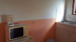 Eine Küche mit Mikrowelle auf einem kleinen Tisch, einem Spülbecken und einem Mülleimer.