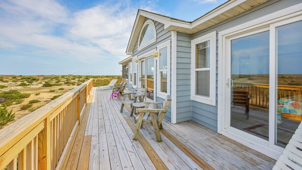 Ein Küstenhaus mit Holzterrasse, großen Fenstern und Blick auf den Strand.