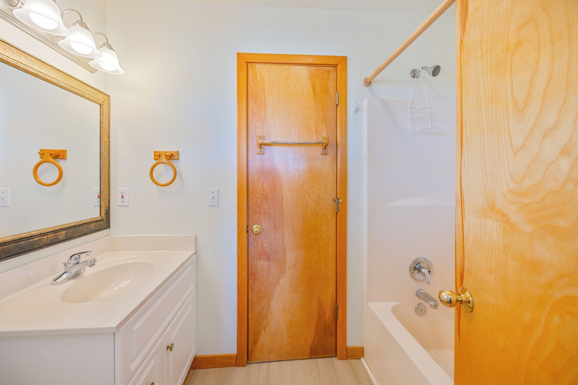 A bathroom with a wooden door, a white sink, a mirror, and a shower area.