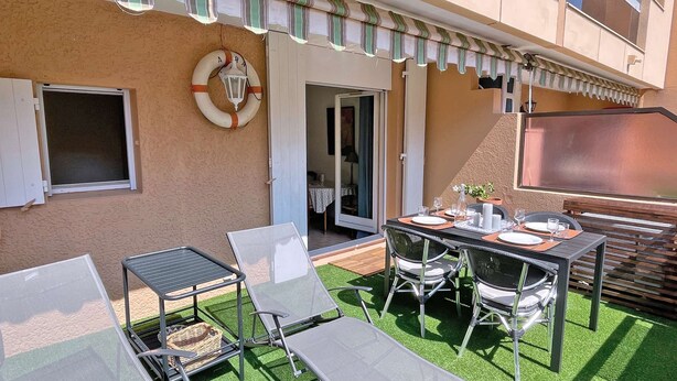 A patio with a table set for dining, outdoor chairs, a small table with a basket, and a lifebuoy on the wall.