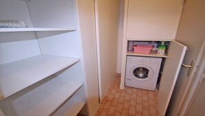 A laundry room with a washing machine, shelves, and a pink basin.