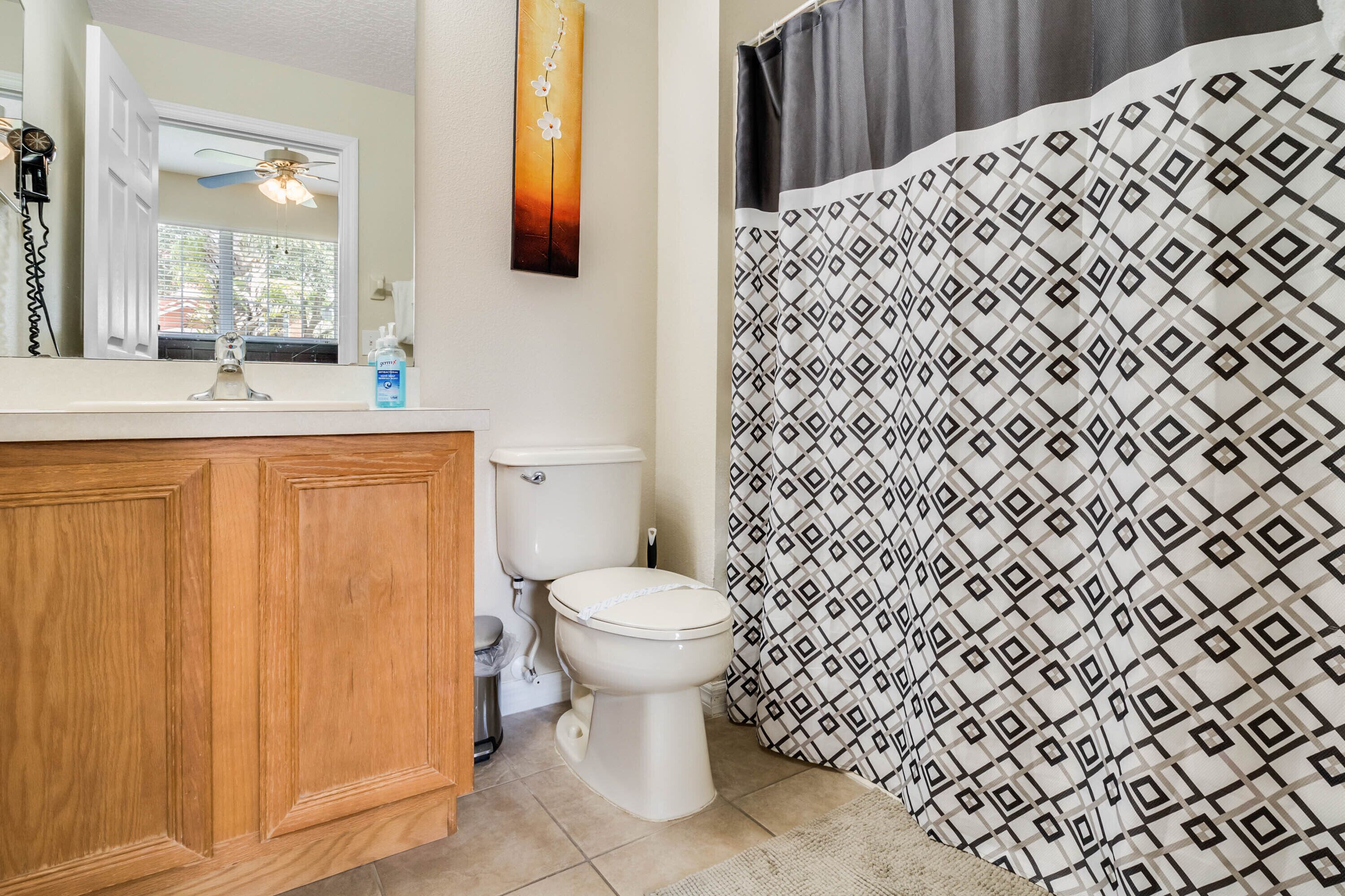 A bathroom with a wooden vanity, a toilet, and a shower curtain with a geometric pattern.