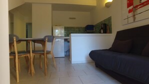 A compact living space with a kitchenette, a dining area with wooden chairs, and a dark-colored sofa. - residence stella d'oro n. 6, f3 a santa giulia (porto vecchio)