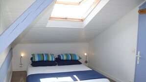 A bedroom with a skylight, a bed with blue bedding, two bedside lamps, and a wooden floor. - Infinity View Bidart (Bidart)