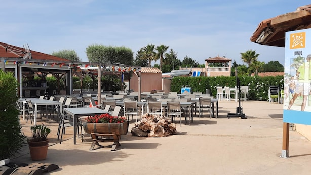 An outdoor patio area with tables and chairs, a barbecue grill, and a wooden planter with flowers.
