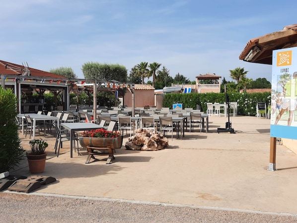An outdoor patio area with tables and chairs, a barbecue grill, and a wooden planter with flowers.