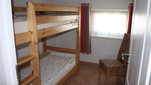A bunk bed with a lower bunk, a chair, a window with curtains, and a tiled floor.