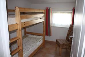 A bunk bed with a lower bunk, a chair, a window with curtains, and a tiled floor.