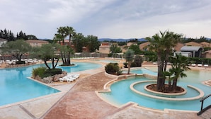 A resort pool area with multiple swimming pools, lounge chairs, and palm trees.