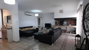 Ein modernes Wohnzimmer mit einer Couch, einem Couchtisch und einem Kamin. Ein Fernseher und ein kleiner Tisch mit Dekorationselementen sind ebenfalls vorhanden.