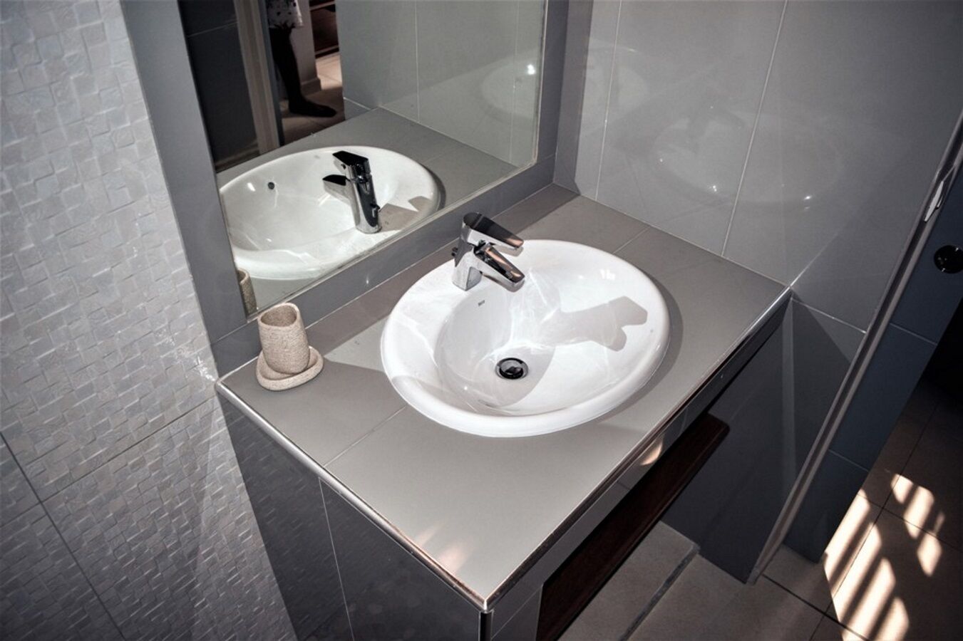 A modern bathroom with a white sink, a mirror, and a towel holder.