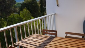 A wooden table and chairs on a balcony with a white railing, overlooking a mountainous landscape.
