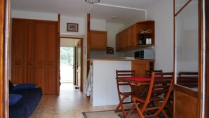 A compact kitchen with wooden cabinets, a dining table with chairs, and a blue sofa in a hallway.