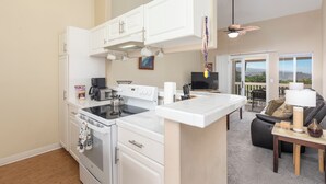 A modern kitchen with white cabinets, a stove, and a dining area with a table and chairs. - 🌴Lovely quiet location partial ocean views.This complex requires a 30 day minimum stay.🌴 (Kailua Kona)