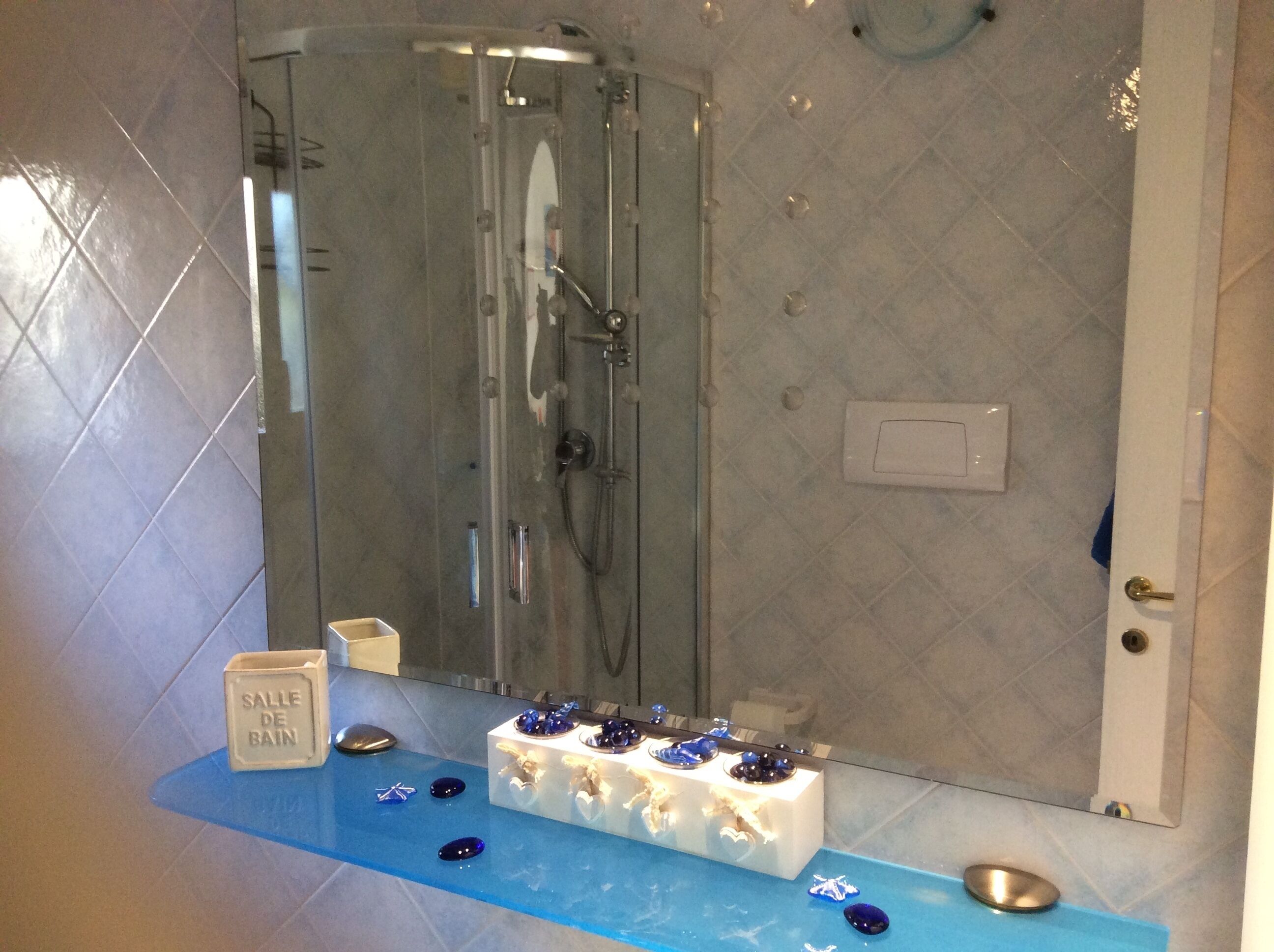 A bathroom with a glass-enclosed shower, a vanity with a mirror, and a blue countertop with decorative items.