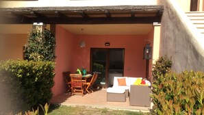 Ein überdachter Patio-Bereich mit Esstisch und Stühlen, einer Couch und einem kleinen Garten mit verschiedenen Pflanzen.