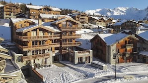 A snow-covered mountain village with wooden buildings, balconies, and a clear view of the mountains in the background. - Appart 130m², full services 4 *, 4 bedrooms, 4 bathrooms / d, south balcony and 2 parking spaces (Montvalezan)