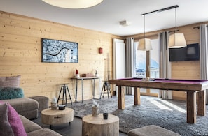 A cozy room with a pool table, wooden walls, a mounted TV, and a large window with a view.