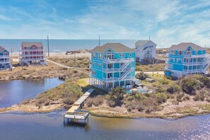 A coastal property with multiple multi-story buildings, a dock, and a small water body. - Premier Soundfront Dog Friendly w/ Pool, Hot Tub, Theater and Game Rooms, More (Hatteras)