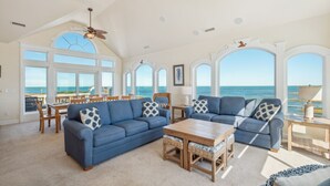 A spacious living room with a large blue sofa, a wooden coffee table, and a ceiling fan. - Premier Soundfront Dog Friendly w/ Pool, Hot Tub, Theater and Game Rooms, More (Hatteras)
