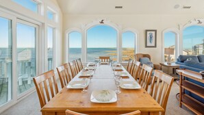 A dining area with a view of the ocean, large windows, and a high ceiling. - Premier Soundfront Dog Friendly w/ Pool, Hot Tub, Theater and Game Rooms, More (Hatteras)