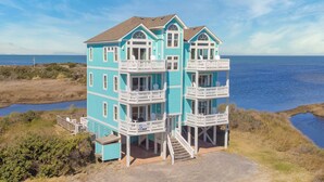 A multi-story coastal house with balconies, a porch, and a view of the ocean. - Premier Soundfront Dog Friendly w/ Pool, Hot Tub, Theater and Game Rooms, More (Hatteras)