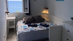 Ein Schlafzimmer mit Bett, Nachttisch, Fenster mit geöffnetem Vorhang, einer Sterndeko und einem gerahmten Bild an der Wand.