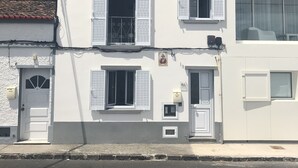 Ein zweistöckiges Gebäude mit weißer Fassade, einem kleinen Balkon im oberen Stockwerk und einer Tür mit einem verzierten Fenster darüber.