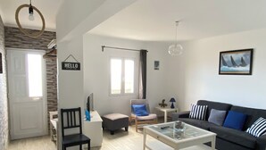 Ein modernes Wohnzimmer mit einer Couch, Couchtisch und Fernseher. An der Wand hängt ein Schild mit der Aufschrift "HELLO" und es gibt ein Fenster mit Vorhängen.
