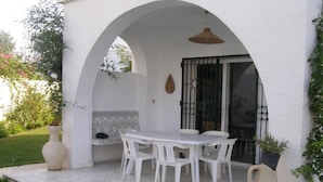 Un patio con una mesa y sillas blancas, un jarrón grande y una planta en maceta.