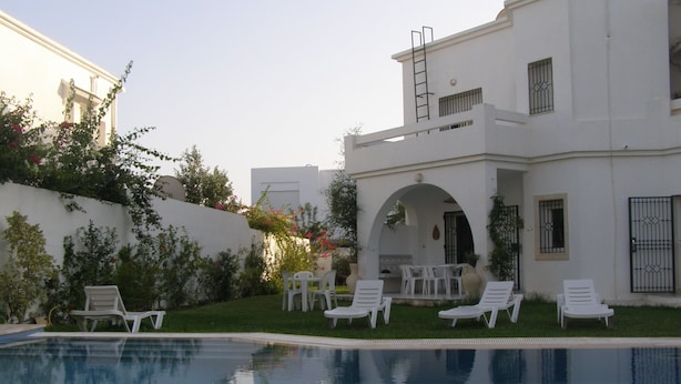 Una casa moderna con piscina, paredes blancas y un patio con sillones de descanso.