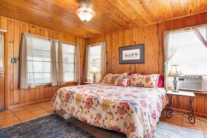 Ein Zimmer mit Holzwandverkleidung, einem Bett, zwei Nachttischen, einem Deckenventilator und einem Fenster mit Vorhängen.