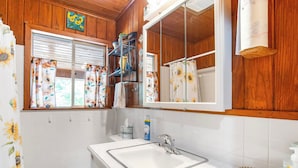 A bathroom with a white sink, wooden cabinets, a mirror, and a shower curtain with a sunflower pattern. - River Ridge Cabin | Bandera Stay with River Access (Bandera)