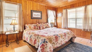A wooden-paneled bedroom with a bed, two bedside tables with lamps, and a window with curtains. - River Ridge Cabin | Bandera Stay with River Access (Bandera)
