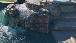 A pool area with a waterfall feature, surrounded by palm trees and a view of distant mountains. - #1 choice in PGA, WOW 3 master bedrm,Huge Private Lot! GR8 Views golf/mt #067336 (La Quinta)