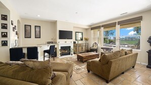 A spacious living room with a fireplace, a television, and a large window offering a view of the outdoors. - #1 choice in PGA, WOW 3 master bedrm,Huge Private Lot! GR8 Views golf/mt #067336 (La Quinta)