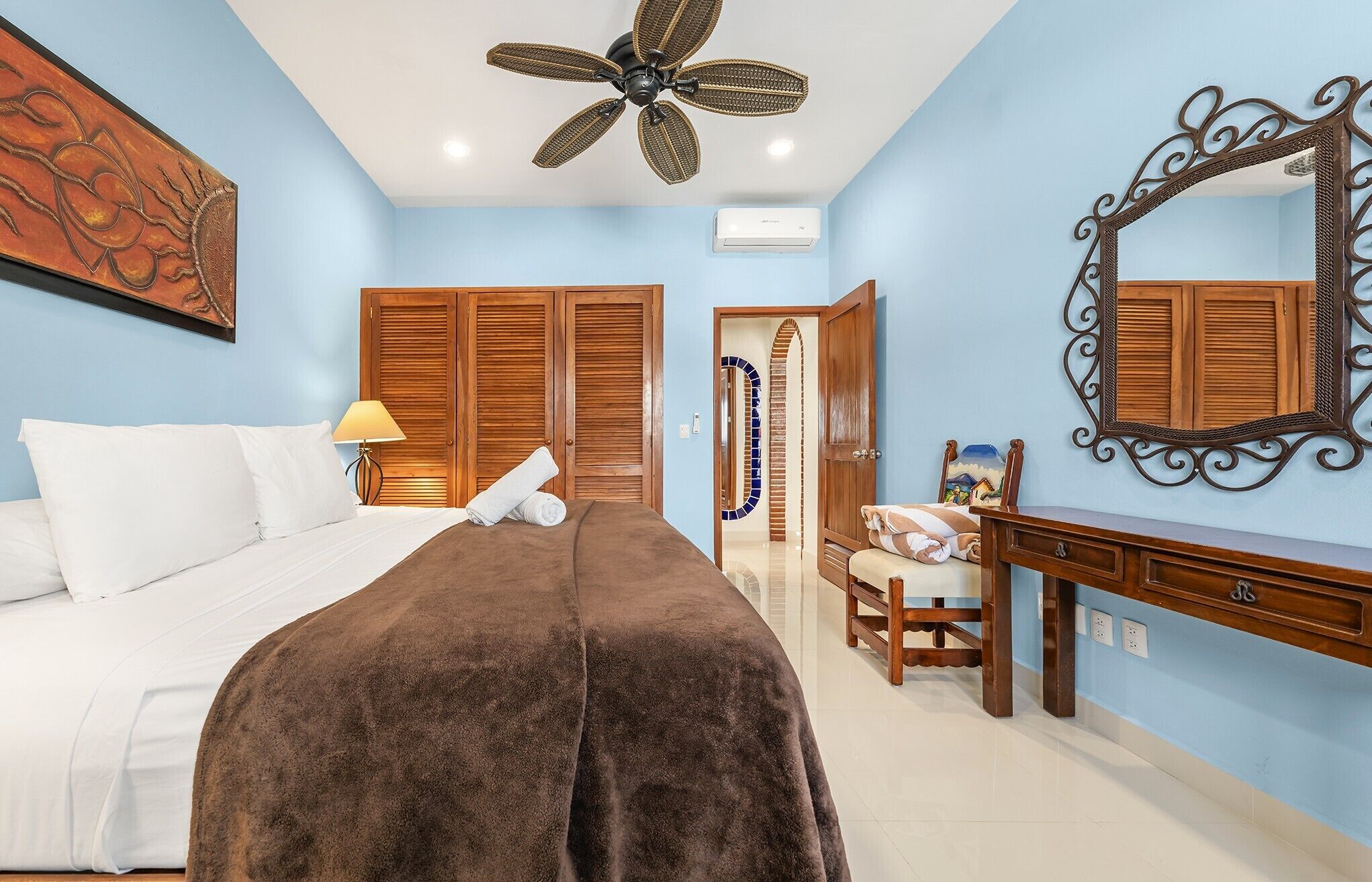 Une chambre d’hôtel équipée d’un lit, d’un bureau, d’une chaise, d’un miroir, d’un ventilateur de plafond et d’un climatiseur fixé au mur.