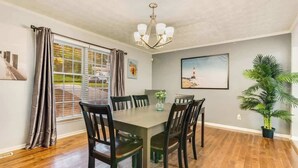 A dining area with a table, chairs, a chandelier, a window with curtains, and a potted plant.